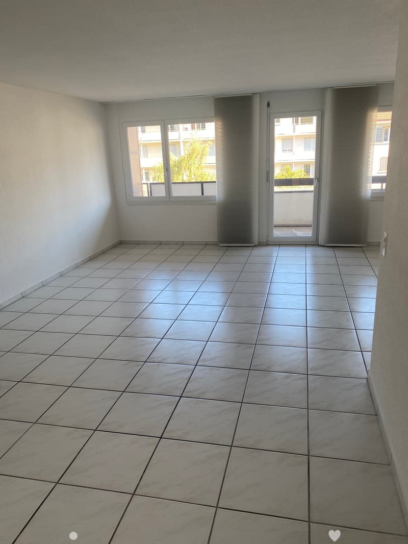 Empty room with tiled floor, white walls, and large windows with a sliding glass door leading to a balcony.