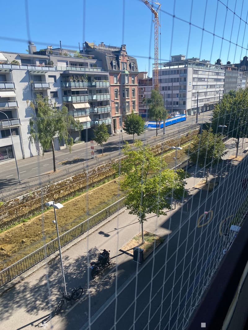Balcony overlooking a city street with modern buildings, trees, a parked motorcycle, and a bicycle.