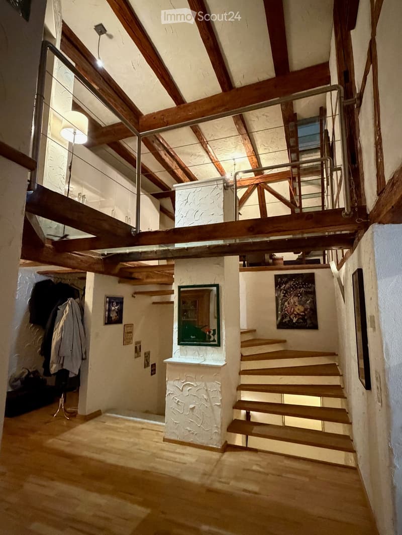 Staircase with wooden steps and metal railing, exposed wooden beams, white textured walls, and artwork on the walls.