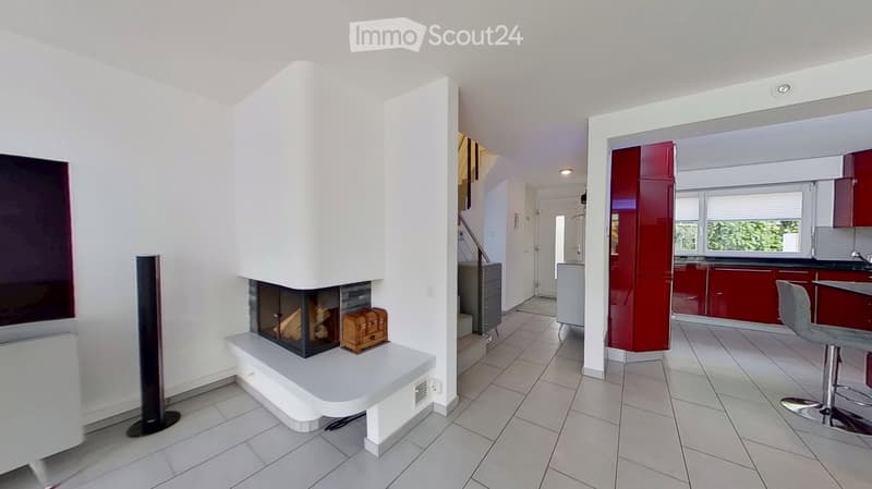 Modern living room with a built-in fireplace, white walls, tiled floor, and a small kitchen area with red cabinets.