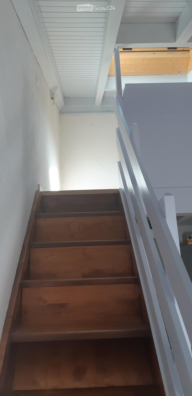 Wooden staircase with white railings and a white ceiling with recessed lighting. The walls are painted white, and the steps are made of polished wood.