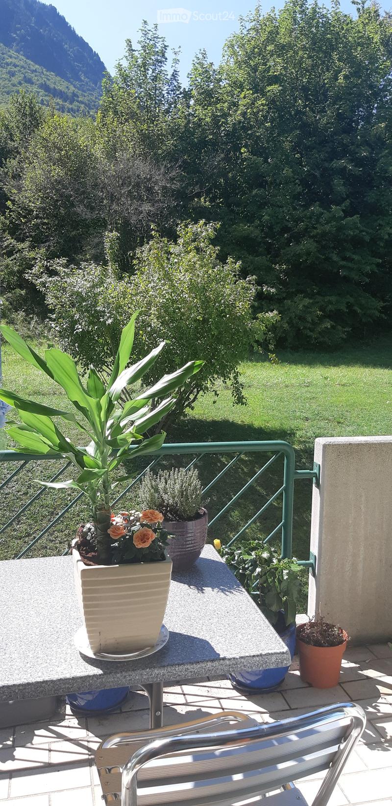 Balcony with a table, potted plants, and a scenic mountain view.
