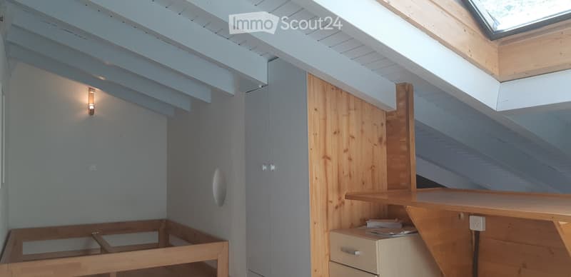 Empty attic room with wooden beams, skylight, and built-in wooden bed frame. No furniture or equipment present.