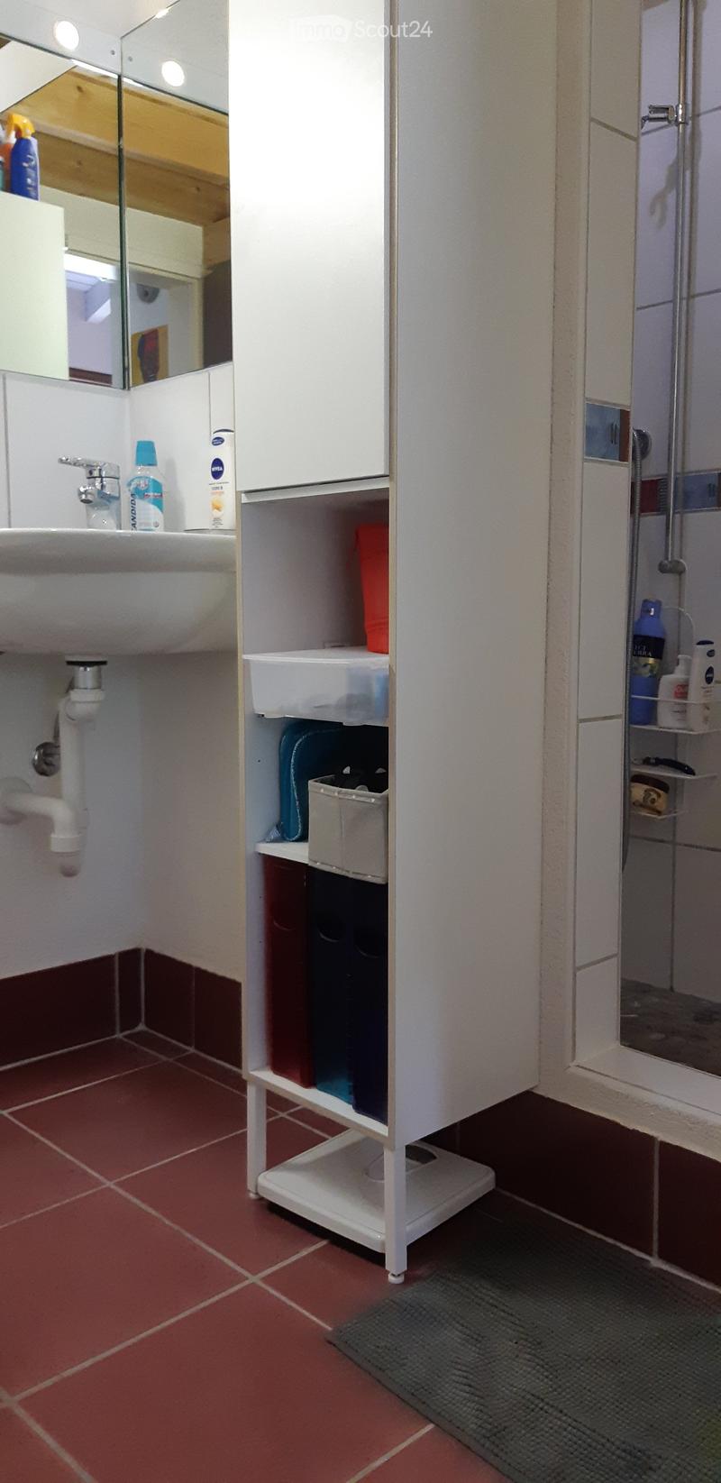 Bathroom with a white sink, mirror, cabinet, and various toiletries. Red tiled floor and walls.