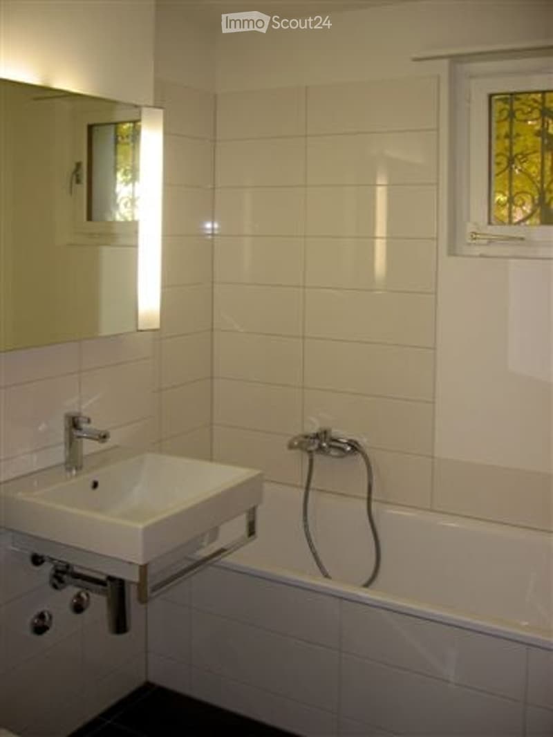 Modern bathroom with white tiled walls, a white sink with a chrome faucet, a mirror above the sink, and a bathtub with a handheld showerhead.