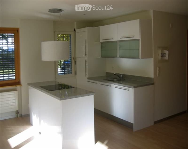 Modern kitchen with white cabinets, a central island, and a pendant light fixture. The space features a sink, faucet, and a window with blinds.