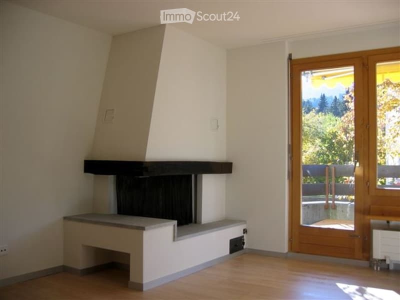 Modern living room with a built-in fireplace, large wooden floor, and large windows offering a scenic view of greenery.