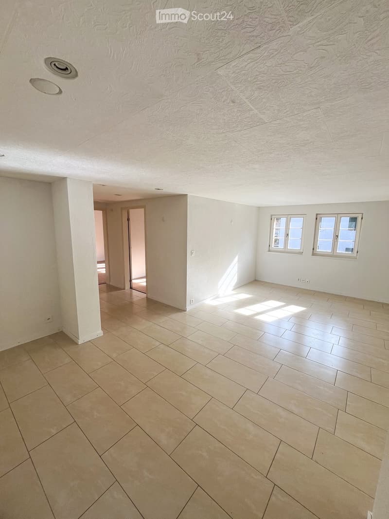 Empty room with light-colored tiled flooring, white walls, and two windows allowing natural light. The ceiling features recessed lighting and a textured finish.