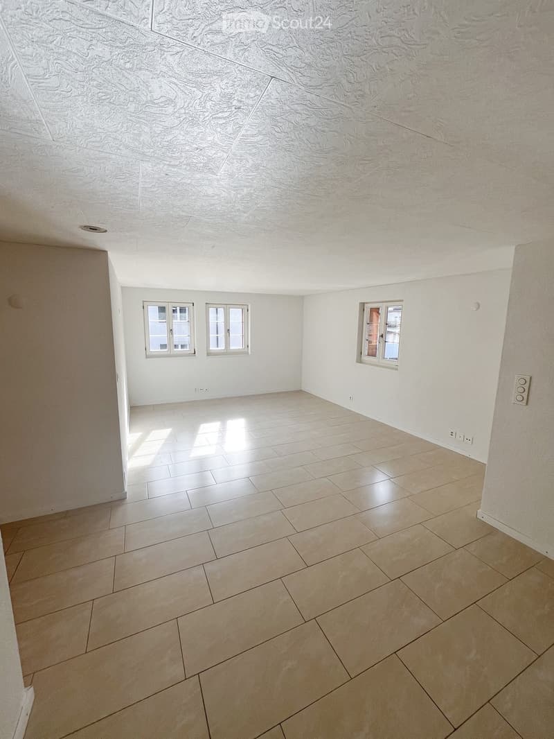 Empty room with light-colored tiled flooring and white walls, featuring three windows and a textured ceiling.