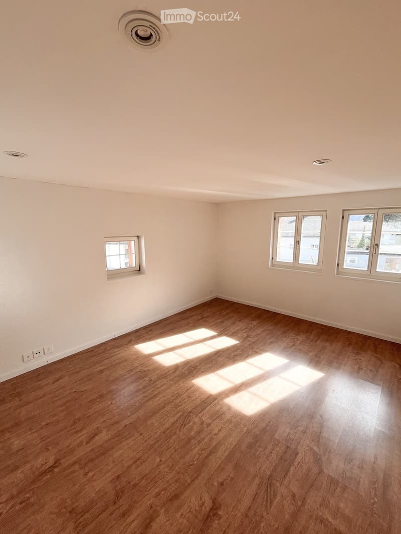Empty room with wooden flooring and white walls, featuring multiple windows allowing natural light to enter.
