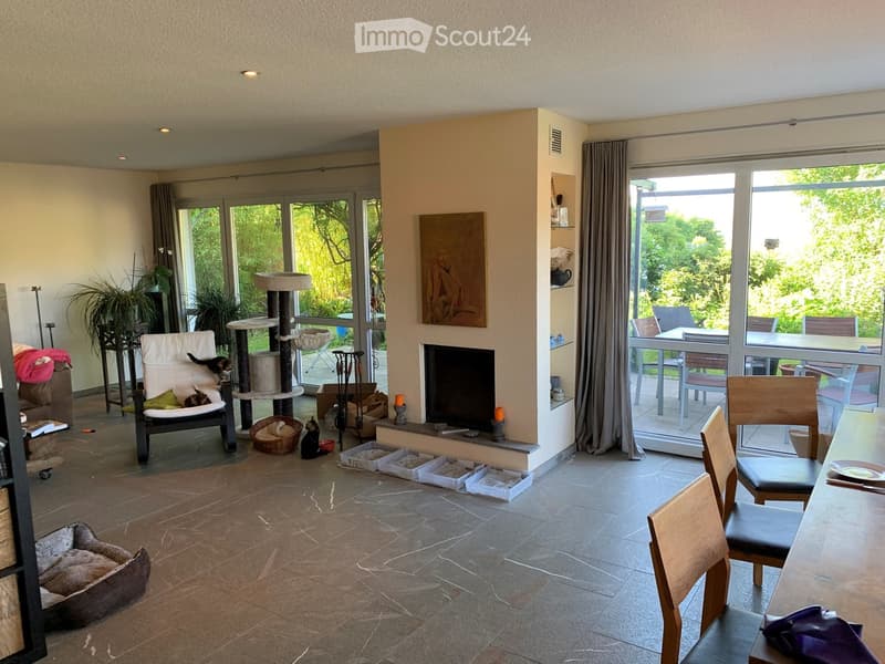 Spacious living room with tiled floor, fireplace, large windows, cat tree, cat bed, sofa, and dining area with table and chairs.