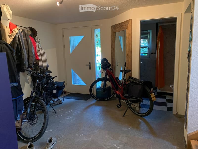 Hallway with tiled floor, two bicycles, coats on a rack, and a partially visible bathroom with a checkered floor.