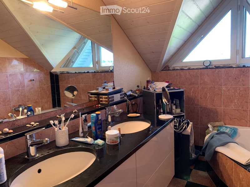 Bathroom with two sinks, mirrors, toiletries, and a bathtub, featuring wooden slanted ceilings and skylights.