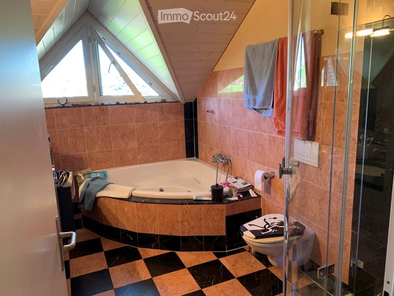 Spacious bathroom with a large bathtub, toilet, glass shower enclosure, and marble tiles. Towels are neatly placed on the edge of the bathtub and near the shower. The room features a skylight window and a checkered black and beige tile floor.
