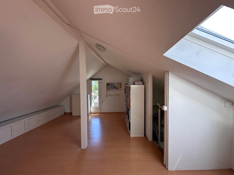 Bright attic space with wooden flooring, slanted ceilings, and built-in storage. Features a bookshelf, a small bench, and a storage cabinet.