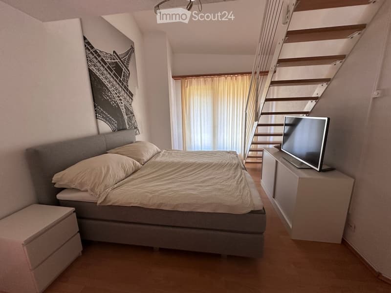 Cozy bedroom with a double bed, nightstand, television, and a staircase leading to another level.
