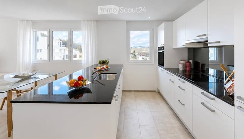 Modern kitchen with white cabinets, black countertops, stainless steel appliances, and a glass dining table with chairs.