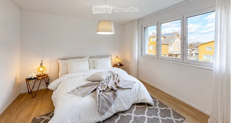 Modern bedroom with a large bed, nightstand, side table, and a hanging ceiling light. The room features wooden flooring and large windows with a view of the neighborhood.