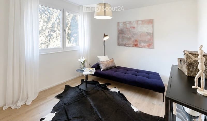 Modern, minimalist living room with large windows offering a view, a dark blue sofa, a coffee table, a floor lamp, and a decorative picture frame on the wall.