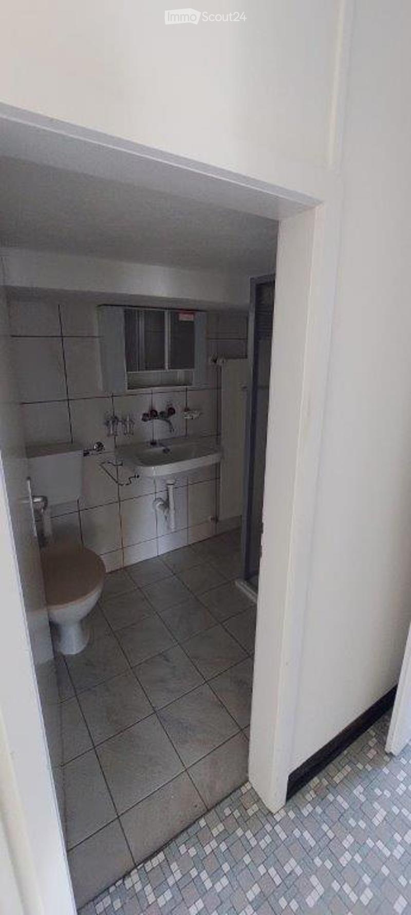 Small bathroom with tiled walls and floor, featuring a toilet, sink with faucet, and a mirrored cabinet above the sink.