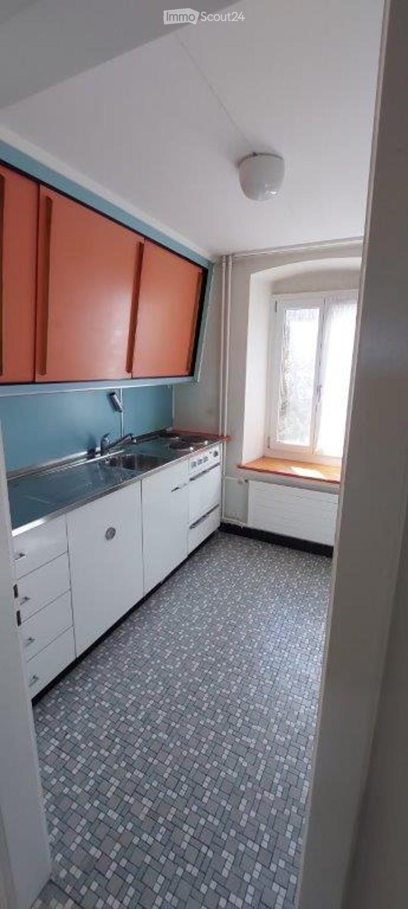 Modern kitchen with white cabinets, stainless steel sink, and tiled floor. Features a window with a wooden sill and a radiator below.