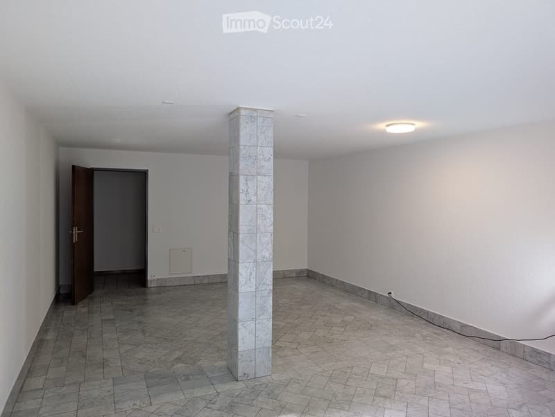 Empty room with white walls, tiled floor, central column, and a single door leading to another space.