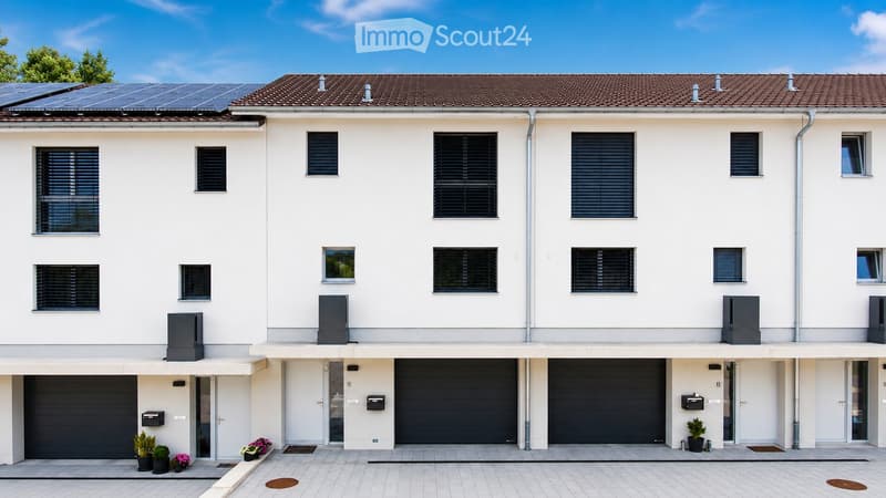 Modern two-story house with white exterior, multiple windows, solar panels on the roof, and three garage doors.