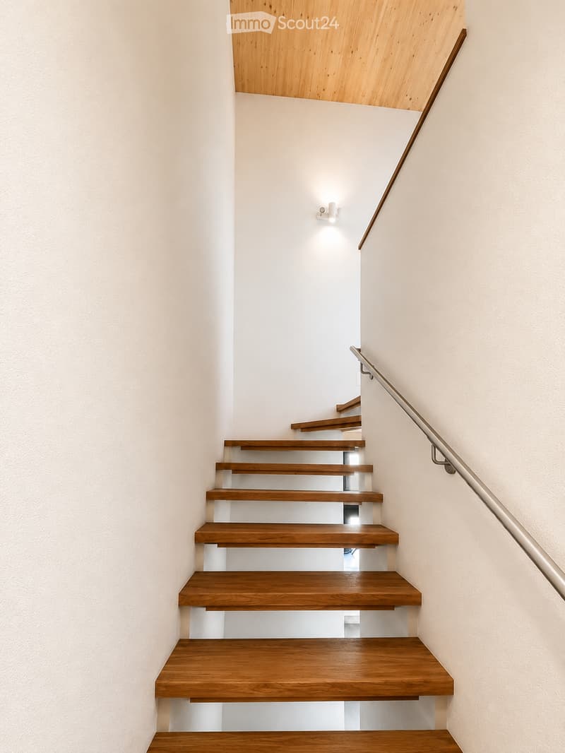 Modern staircase with wooden steps and a sleek metal handrail, illuminated by recessed lighting.