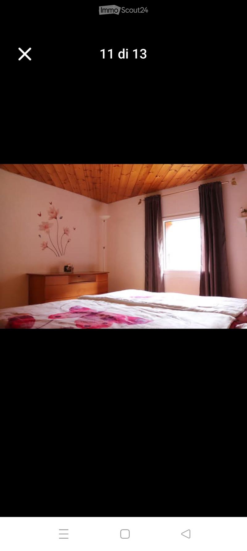 Bedroom with a wooden ceiling, a bed with floral bedding, a nightstand, and a window with dark curtains.
