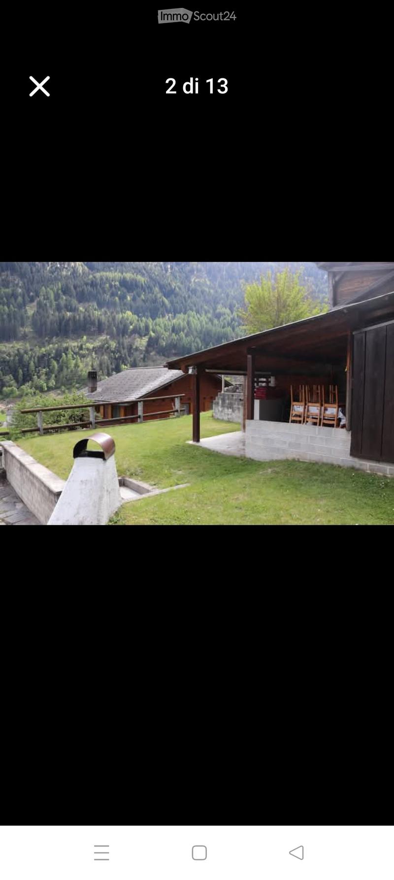 A grassy outdoor area with a wooden deck, chairs, and a scenic mountain view in the background.