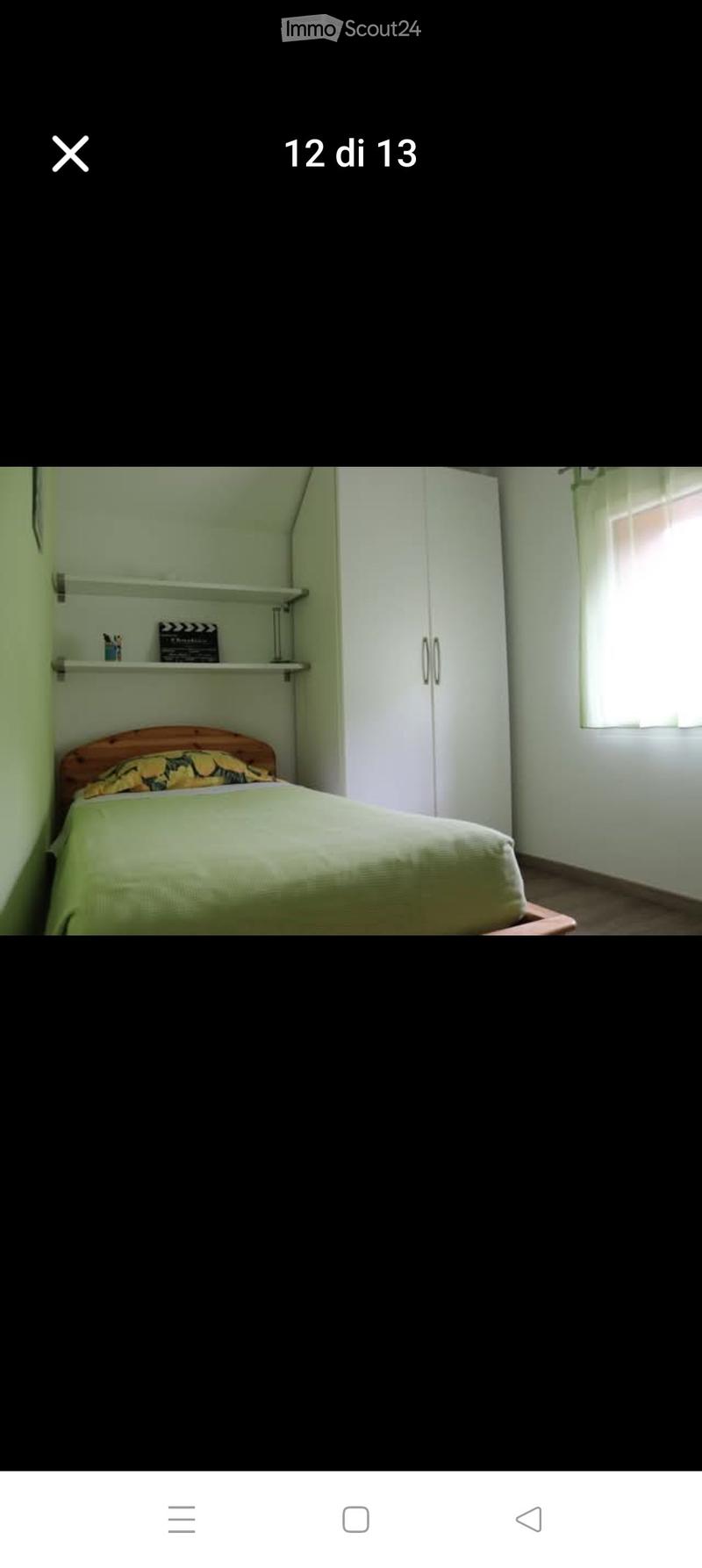 Bedroom with a single bed, green bedding, a white wardrobe, and a small shelf with a few items.