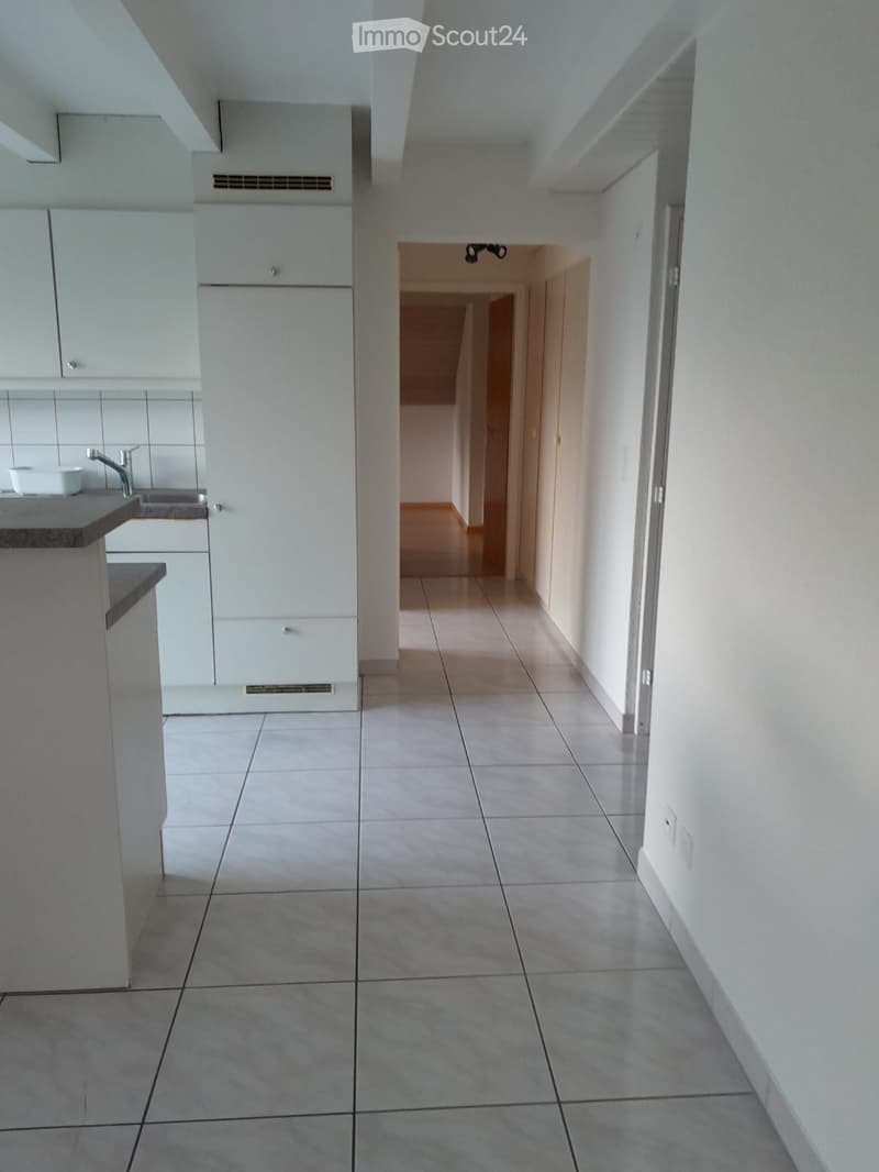 A clean, modern hallway with tiled flooring and white walls, leading to a kitchen area with white cabinets and a countertop.