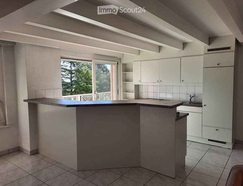 Modern kitchen with white cabinets, a central island, and a large window offering a view of greenery outside.