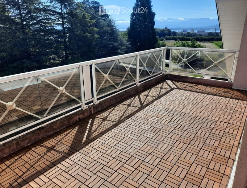 Balcony with wooden decking, glass railing, and scenic view of trees and water.