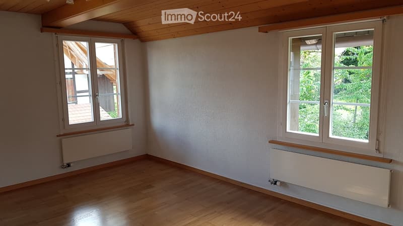 Empty room with wooden flooring, white walls, and large windows with radiators beneath them. The ceiling has exposed wooden beams.