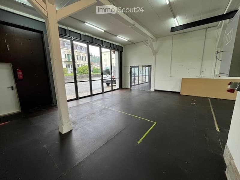 Empty warehouse, black floor, white walls, glass windows, emergency exit, fire extinguisher, white ceiling lights, two doors