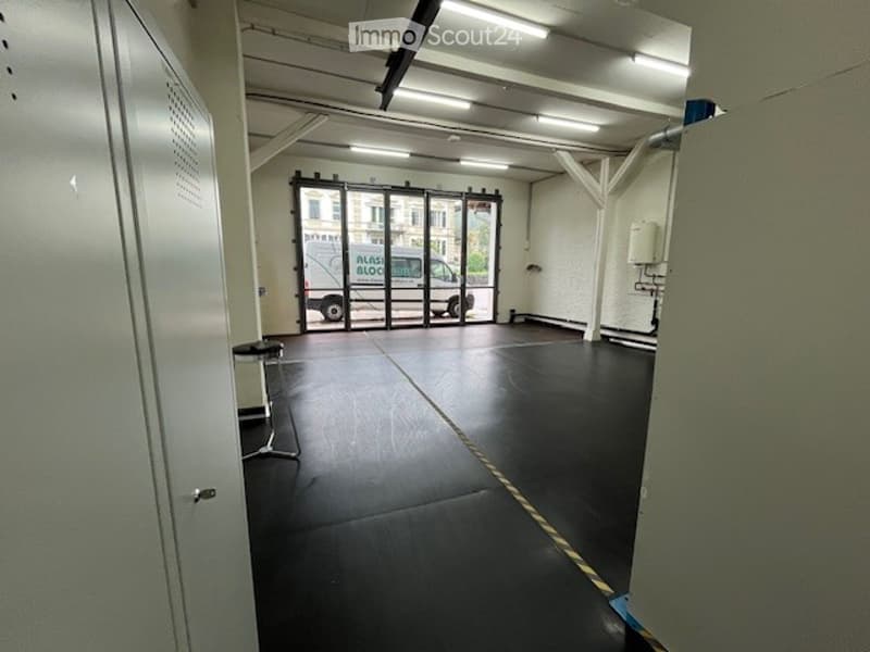 Empty room with black flooring, white walls, ceiling lights, glass doors, entrance, table with stool, utility box, van outside