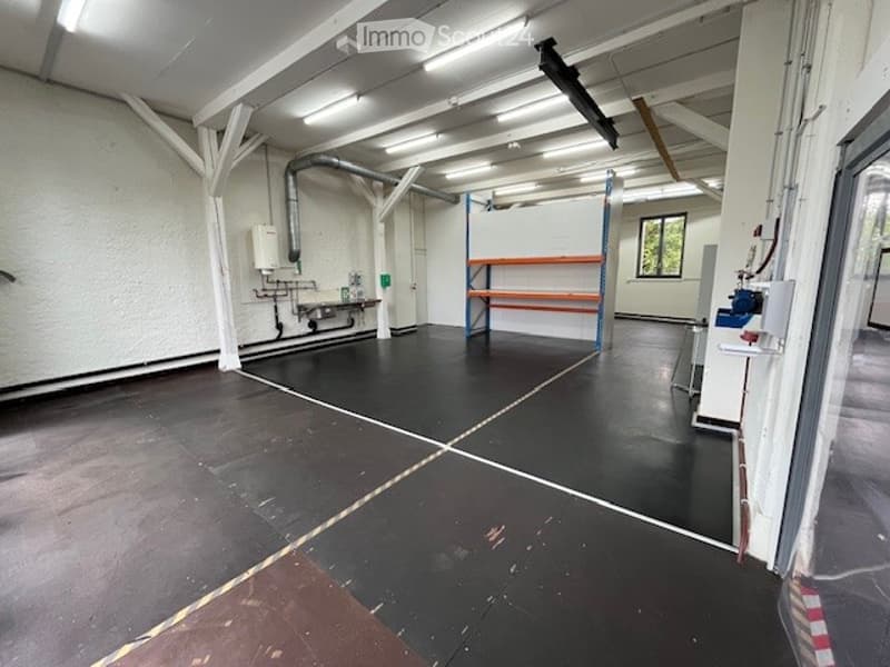 Large open room, industrial style, black flooring, metal beams, white walls, pipework, shelving, windows, doors