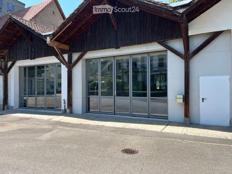 Two-story building with large glass doors, black roof, white walls, parking area, and a white door.