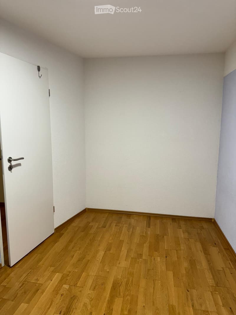 Empty room with wooden flooring and white walls, featuring a white door with a silver handle on the left side.