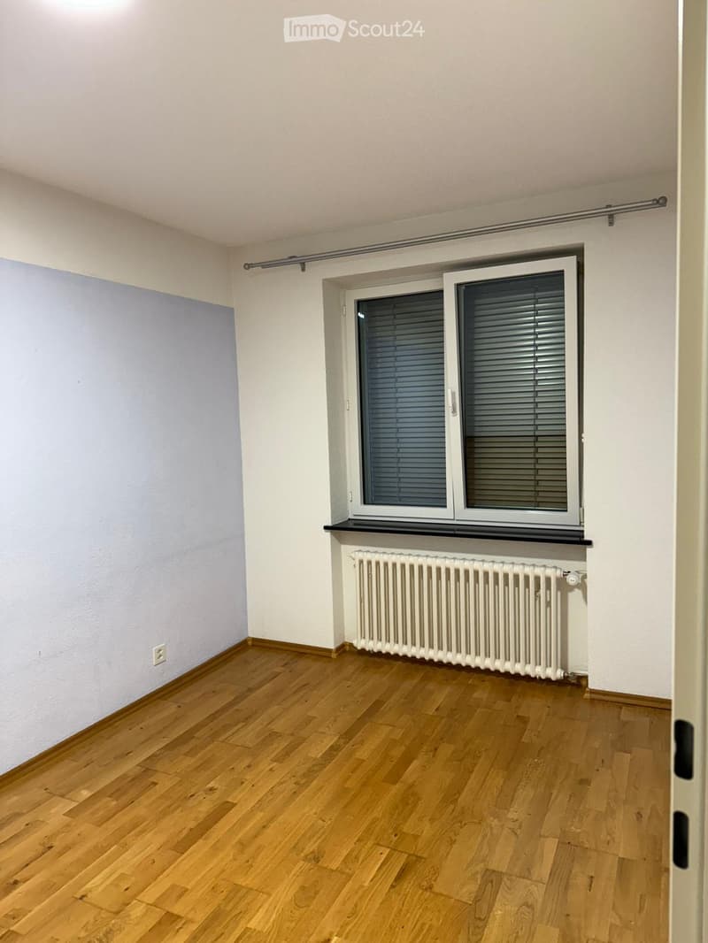 Empty room with wooden flooring, white walls, a window with blinds, and a radiator below the window.
