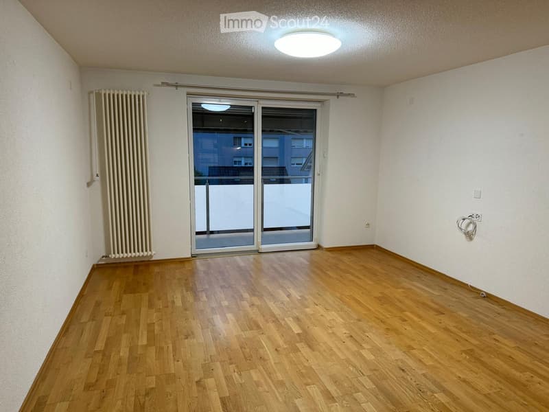 Empty room with wooden flooring, white walls, and a sliding glass door leading to a balcony.