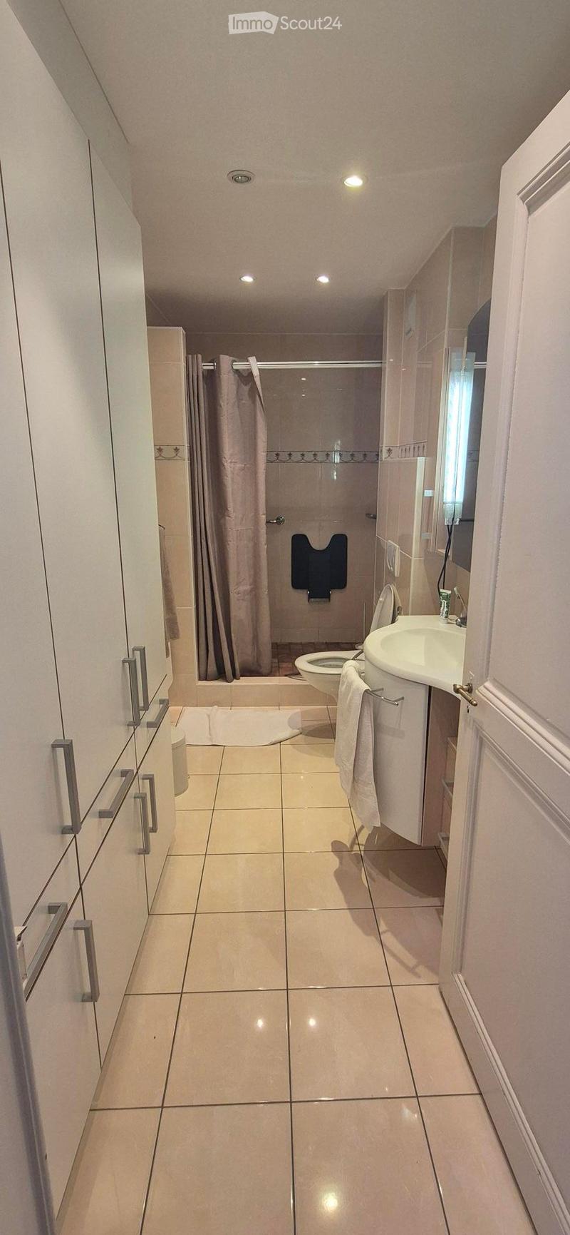 Modern bathroom with tiled floors and walls, featuring a toilet, sink, mirror, and shower area with a curtain.