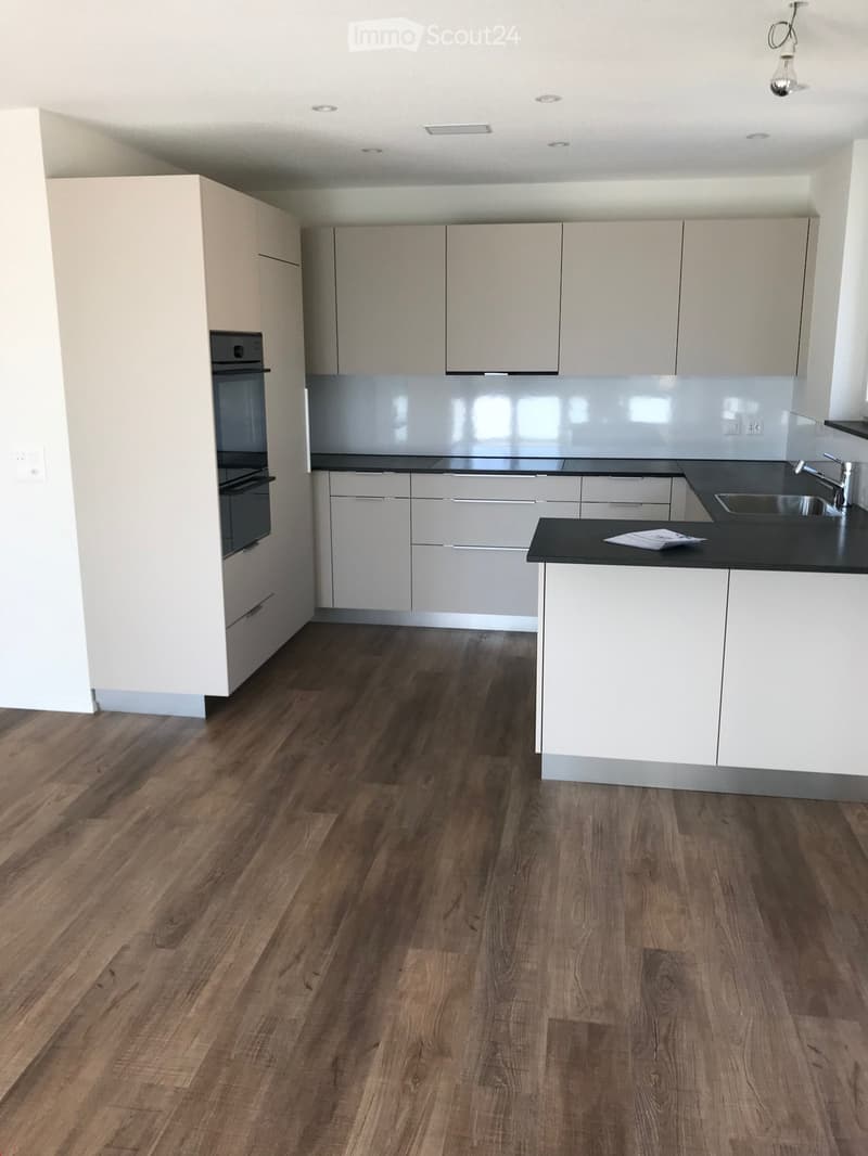 Modern kitchen with white cabinets, black countertops, and wooden flooring. Features an oven, sink, and faucet.
