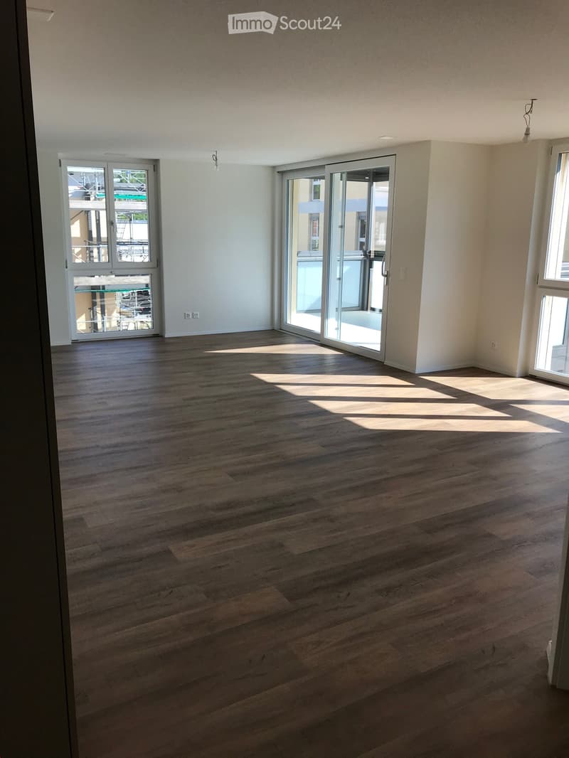 Empty room with wooden flooring, large windows, and sliding glass doors leading to a balcony.