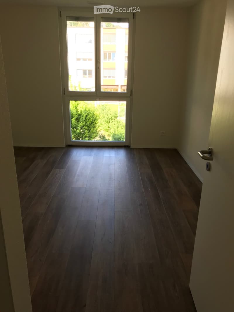 Empty room with wooden flooring and large sliding glass doors leading to a balcony or outdoor area. The walls are painted a light neutral color, and the space is well-lit with natural light.
