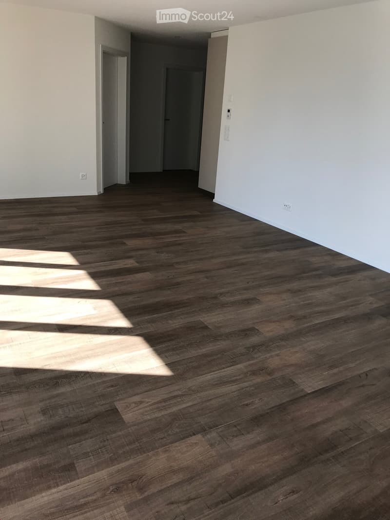 Empty room with wooden flooring and white walls, featuring two open doorways leading to adjacent spaces.