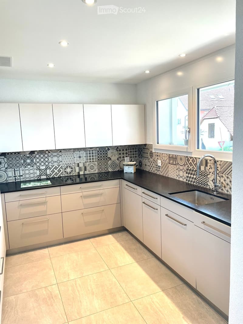 Modern kitchen with white cabinets, black countertop, and a decorative backsplash. Features a sink with a modern faucet and a small appliance on the counter.