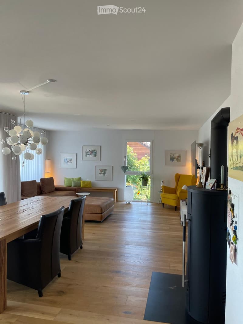 Open-plan living and dining area with wooden flooring, a large chandelier, a sofa, a dining table with chairs, and a yellow armchair.