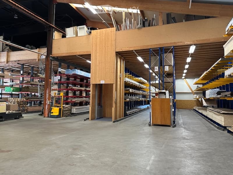Warehouse with exposed wooden beams, metal shelving units, and various construction materials stored on shelves and pallets.